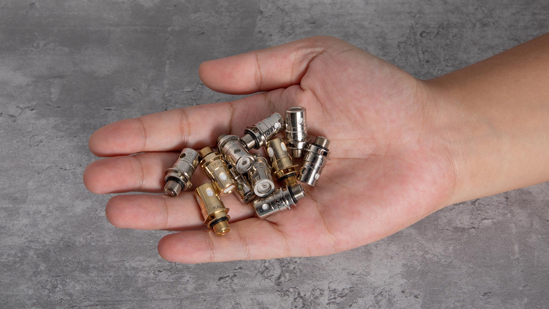 Das Bild zeigt eine Hand, die mehrere Vape Coils aus verschiedenen Metallen und Designs hält. Diese Spulen sind wesentliche Bestandteile von Vaping-Geräten und demonstrieren die Vielfalt und Innovation der Vaping-Technologie.