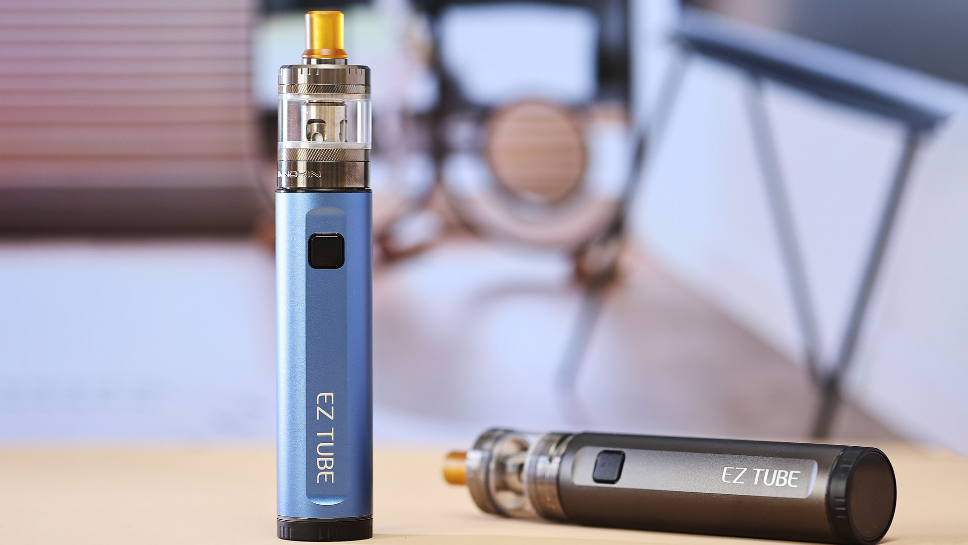 Eine Nahaufnahme von zwei EZ TUBE Vape Pens auf einem Tisch, einer aufrecht stehend in blauer Ausführung und der andere waagerecht liegend in einem dunkleren Farbton, zur Veranschaulichung gängiger Probleme bei der Fehlersuche, wenn ein Vape Pen nach dem Aufladen nicht funktioniert, z. B. wenn das Gerät den Pod oder die Patrone nicht erkennt.