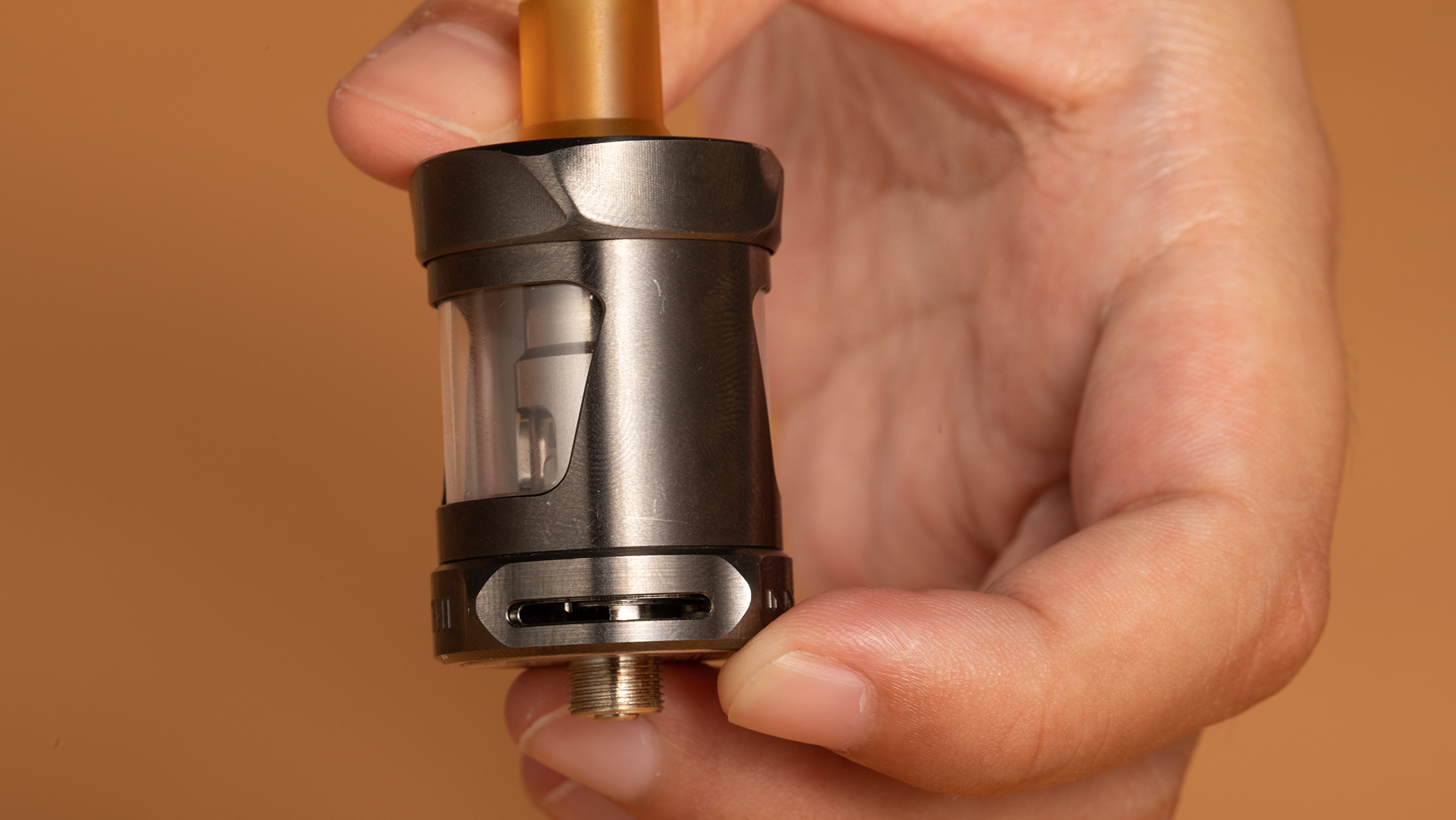 Eine Nahaufnahme einer Hand, die einen Vape-Tank mit einer sichtbaren Spule im Inneren hält, die das untere Gewinde und den Anschluss zeigt. Das Bild konzentriert sich auf den Tank als Teil der Fehlerbehebung Schritte für die Behebung der "No Atomizer" Fehler, wenn der Tank oder Pod hat ein Problem.