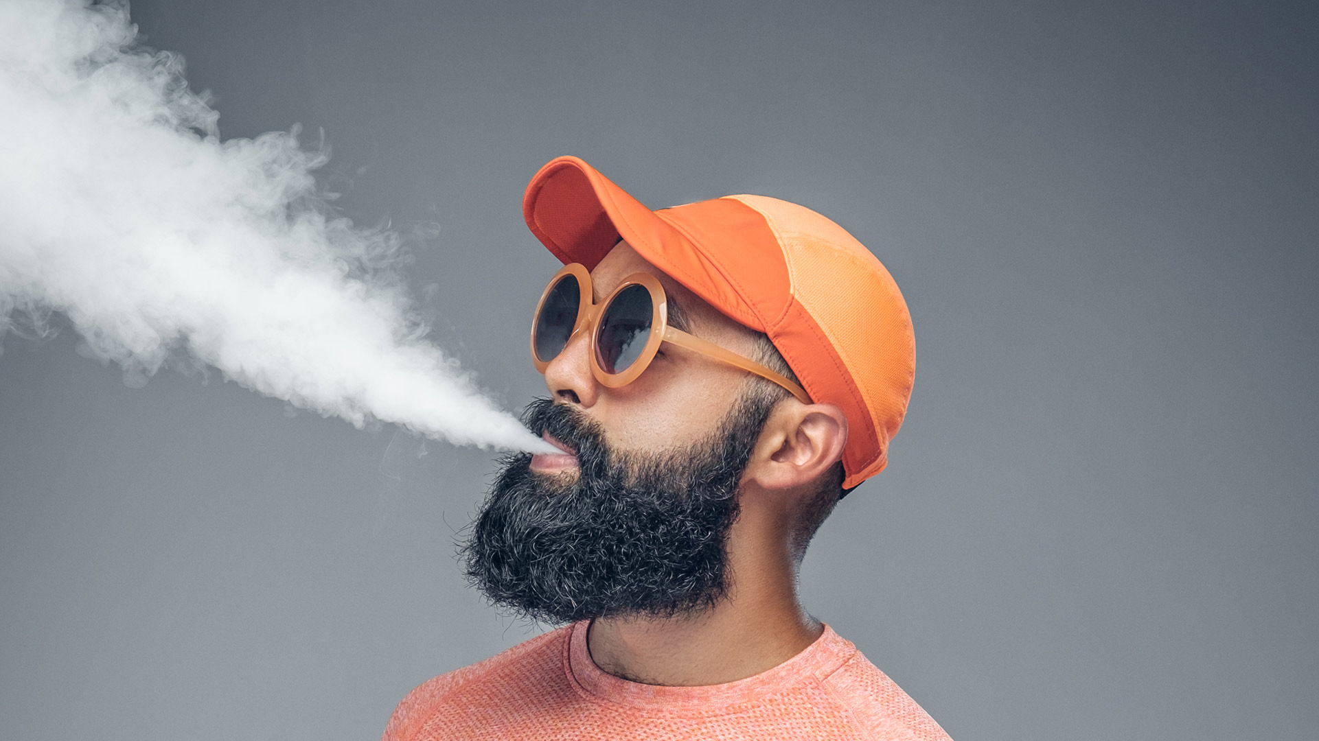 Ein Mann mit einem orangefarbenen Hut und einer Brille raucht.