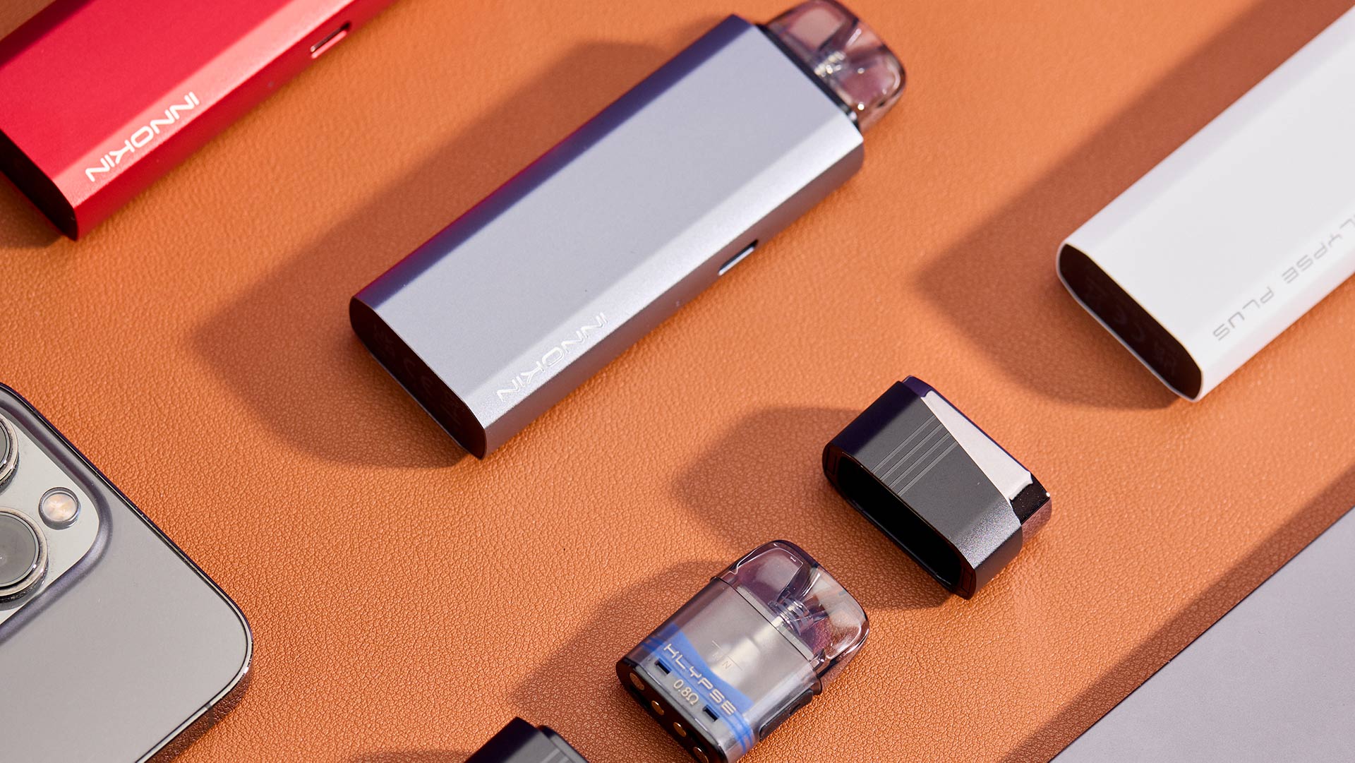 Innokin Klypse Pod-System in verschiedenen Farben, präsentiert auf einer strukturierten orangefarbenen Oberfläche.